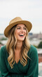 © Inspire Shots Hub - Woman with blonde hair wearing a straw hat and green dress, laughing joyfully, showcasing happiness and a carefree attitude for summer lifestyle concepts