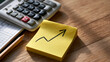 © Denis Yevtekhov - Yellow sticky note carrying a simple rising business growth chart beside a white calculator quarterly ledger and a sharpened pencil aligned beneath the note light oak desk with