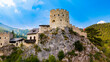 © Vadim - A crenellated Austrian castle keep stands on a rocky outcrop.. Tan masonry and dark roof tiles rise above gray rock, with green woodland and mountains behind.