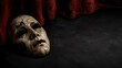 © Milan - Antique cracked drama mask resting on dark stage floor. Theatrical red velvet curtain backdrop. Tragedy and acting concept