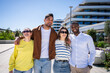 © CarlosBarquero - Multicultural group of friends stand close together and smile outdoors in a clean modern neighborhood with contemporary architecture and blue sky.
