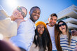 © CarlosBarquero - Five friends pose closely for a low angle selfie outdoors in a bright residential neighborhood, showing diversity, friendship and cheerful social connection.
