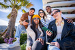 © CarlosBarquero - Five multicultural friends sit together and smile with phones in hand, enjoying leisure time and digital connection in a sunny residential district.