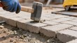 © Наталия Пилипенко - A close-up view of a worker in gloves using a mallet to level concrete paving blocks during sidewalk installation and outdoor construction work at a building site
