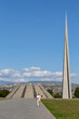 © Eric Lafforgue - Man carrying a flower while walking beneath the tall spire and stepped pyramid with the city skyline and hills visible in the background near the memorial complex, Yerevan, Armenia