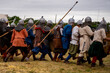 © Marina - Participants in medieval armor and helmets move across a grassy field carrying spears during a historical reenactment.