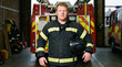 © ADDICTIVE STOCK - Firefighter holding helmet in fire station with fire engine