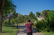 © Laura - Photograph from a rear perspective of a young man walking along a park path while listening to music with headphones.