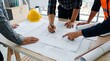 © CuteBee - Architects and engineers reviewing building blueprints on table with yellow hard hat in construction site office for collaborative professional planning and team project management work