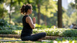 © Denis Yevtekhov - Young Indian woman practicing yoga in a leafy park medium rear view of a steady seated posture with palms joined at chest height and face turned away simple activewear on a mat