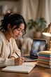 © Gfxbyus - Student studying at home with laptop and stack of books under warm lamplight