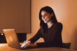 © Daniel - Work continues late at night as woman types on a laptop at a wooden desk. The freelancer handles online business tasks through warm screen light in a personal home workspace with steady productivity.