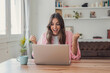 © Daniel - Woman celebrates a successful work result on her laptop at home, raising clenched fists with excitement. Remote office scene conveys freelance business achievement, good news and productivity.