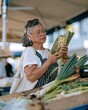 © Ryzhkov - Senior woman holding a squash at an outdoor market, choosing organic vegetables with a natural, thoughtful expression for healthy living