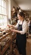 © silva - Woman in apron arranging handmade soaps in a rustic shop with natural light
