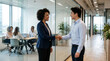 © Virginia - Diverse business people shaking hands in a modern glass office corridor as colleagues work in the background
