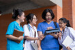 © Prot - Asian healthcare students gather outside a university building to review information on a tablet, combining teamwork, medical education, technology, and friendly campus interaction.