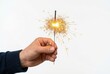 © trimiati - Hand Holding a Burning Sparkler with Golden Sparks Isolated on White Background for Celebration and Festive Events