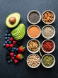 © mglgilang - Top view of various healthy superfoods including fresh berries avocado nuts seeds and legumes on a dark background.