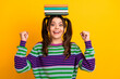 © deagreez - Young woman with colorful striped sweater balances a stack of books on her head in yellow studio for a playful fashion lifestyle energy education