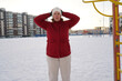 © Ирина Старикова - Front view of a mature woman in red jacket warming up at snowy public sports ground in winter.