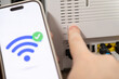 © Alina - A hand presses the wireless button on a home router while a smartphone screen displays a successful internet connection icon to represent easy network setup and digital connectivity