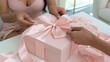 © Nattapol - Hands tying silk ribbon on blush gift box, creating elegant present with care and affection in bright home setting