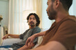 © eggeeggjiew - Two Asian men sit together and talk at home with relaxed and eye contact, showing friendship, communication, companionship and social connection.