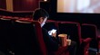 © Aliaksandra - Digital distraction, A solitary viewer illuminated by a glowing handheld device in a dark cinema