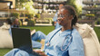 © DC Studio - Medical student studies independently on a laptop while reclining on a beanbag in a sunny modern campus courtyard, with classmates softly blurred in the background during solo study.