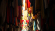 © Abderrahmane - Colorful clothes and fabrics hanging in narrow market alley with sunlight beams, vibrant textile souk atmosphere