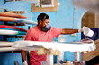 © peopleimages.com - Workshop, PPE and black man with surfboard, fiberglass and creative for talent and hobby skills. Craftsman, artist and repair with respirator for design, manufacturing and custom work for artisan