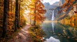 © Vera D - Scenic path overlooks an alpine lake and narrow waterfall framed by colorful autumn trees and distant mountains, in seasonal light