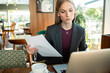 © Davor - Businesswoman reviewing document while working on laptop in cafe