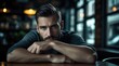 © Natalia - A pensive handsome man with a beard sits at a dark table inside a moody bar looking forward. Confident masculine styling portrait display backdrop layout. States of mind theme.