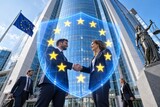 Na pierwszym planie cyfrowa tarcza z motywem flagi UE. Przez tarczę widać pracowników korporacyjnych podających sobie ręce na tle przeszklonego wieżowca sądu. Koncept zgodności prawnej i korporacyjnej