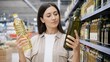 © Jafree - Woman choosing product at store comparing options between cooking oils on shelves, concept of shopping decision-making evaluation, consumer behavior grocery shopping supermarket choice