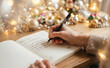© Nina - Woman writing New Year resolutions in a notebook on a wooden table with festive Christmas lights and holiday decorations
