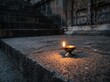 © LuckyFH - A Gentle Glow of Hope: A small oil lamp flickers warmly on an ancient stone step, its flame casting a soft light against the dark, weathered stone and ornate carvings.