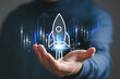 © Bordinthorn - Digital startup growth concept showing a glowing rocket launching above a business skyline from an open hand, symbolizing innovation, entrepreneurship, technology, investment, progress, future success