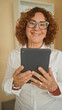 © Krakenimages.com - Woman holding tablet with both hands, smiling while wearing glasses and white shirt inside building; confidence connection.