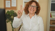© Krakenimages.com - Woman shows peace sign with right hand by a computer, wearing glasses and a white shirt in a building office; joy positivity warmth connection.