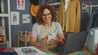 © Krakenimages.com - Woman dressmaker holding smartphone, hand to chest beside laptop, sewingmachine, measuring tape and fabric sketches on table in studio; gratitude creativity.