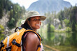 © CarlosBarquero - A Latina African American woman looks back over her shoulder and smiles, wearing a broad brimmed hat and yellow hiking backpack. Photographed in the Aiguestortes area of the Spanish Pyrenees.