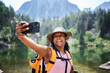 © CarlosBarquero - A Latina African American woman holds a mobile phone at arm's length and smiles while taking a selfie beside a mountain lake. Photographed in the Aiguestortes area of the Spanish Pyrenees.
