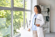 © Pixel-Shot - Healthcare professional and medical career, female doctor standing in office with clipboard looking out window for patient care and wellness