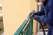 © Александр Марченко - Worker sanding old balcony railing with power tool