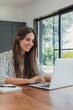 © Daniel - Woman shops online with a laptop at a wooden table, using the trackpad beside a notebook. Smiling customer explores ecommerce, online retail and digital payment options from home in daylight.