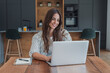 © Daniel - Woman manages home finances on a laptop at her kitchen table, typing beside a notebook. Home finances, budgeting and digital banking support household money management in a bright home office.