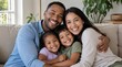 © Patrick - Cheerful multiethnic parents and two young children hugging together on soft beige sofa, smiling directly at camera, happy family bonding at home, warm natural light - detailed commercial stock